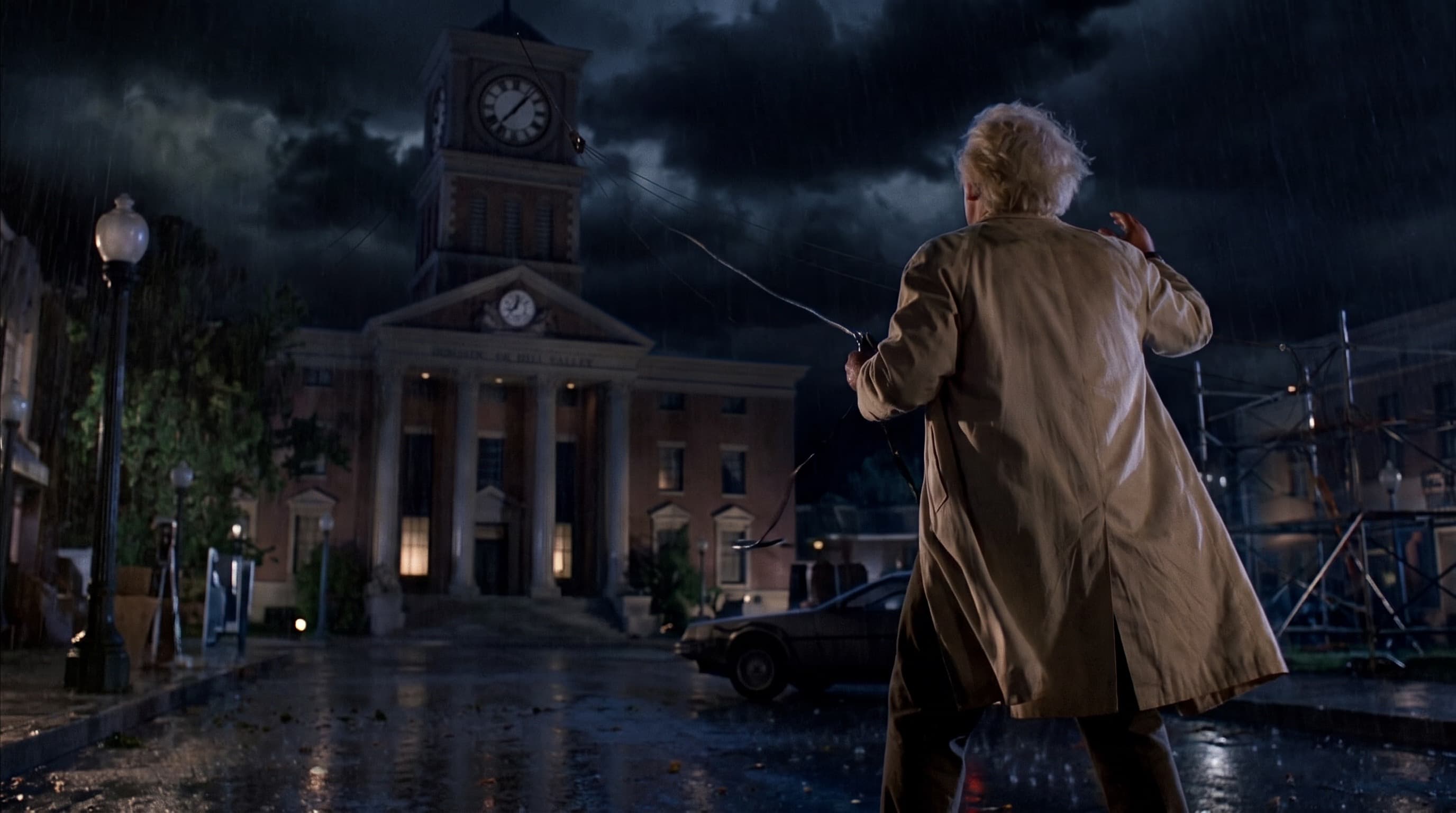 Doc Brown in the rain in front of the Hill Valley courthouse clock tower, holding the cable, as the storm gathers.